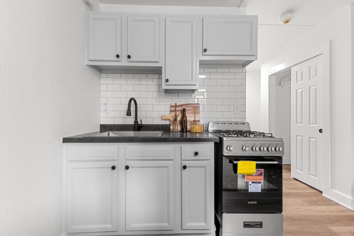 The kitchen with white shaker cabinets, a gas range, subway tile backsplash and a dark countertop.