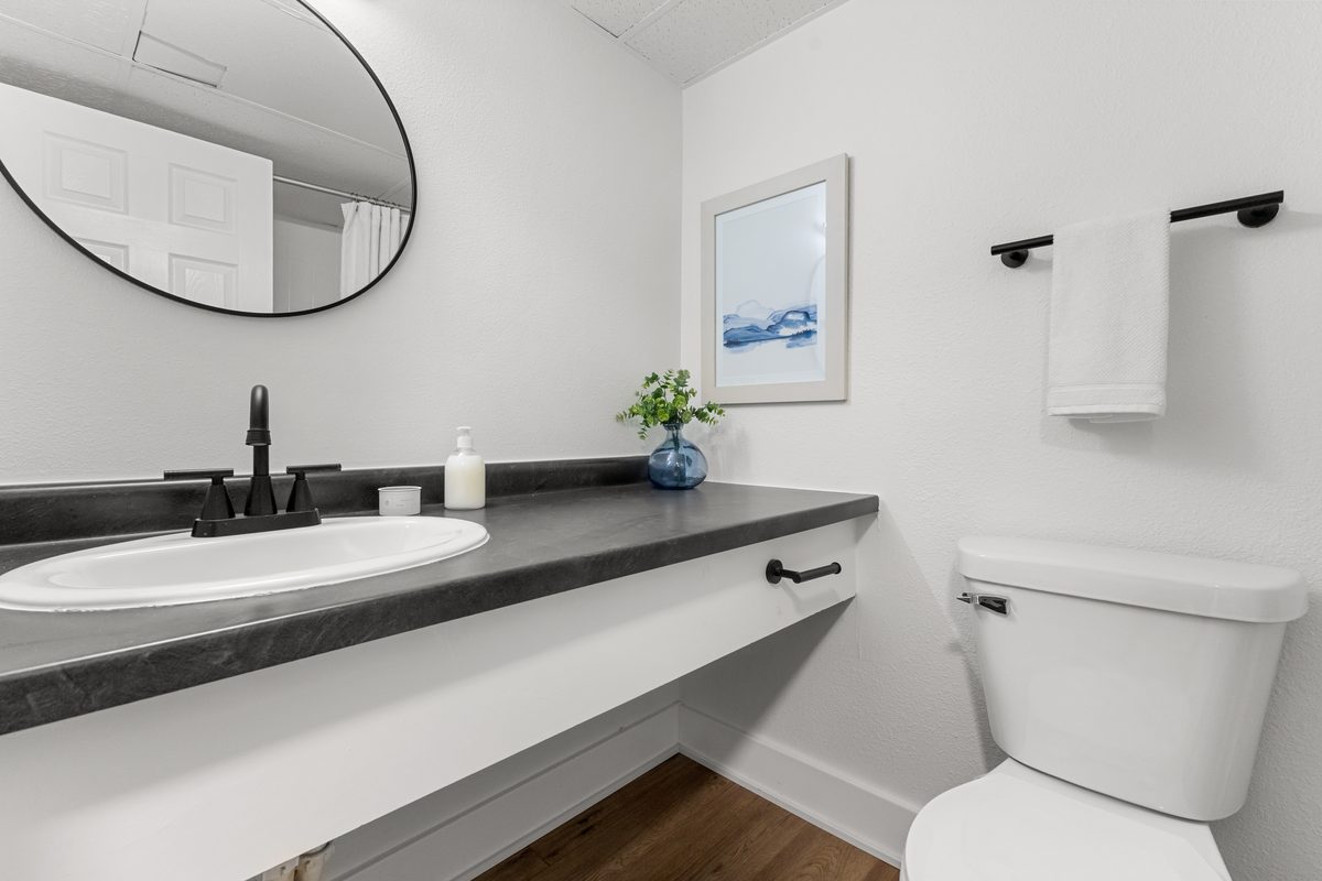The bathroom vanity with a round mirror, black fixtures and a dark countertop.