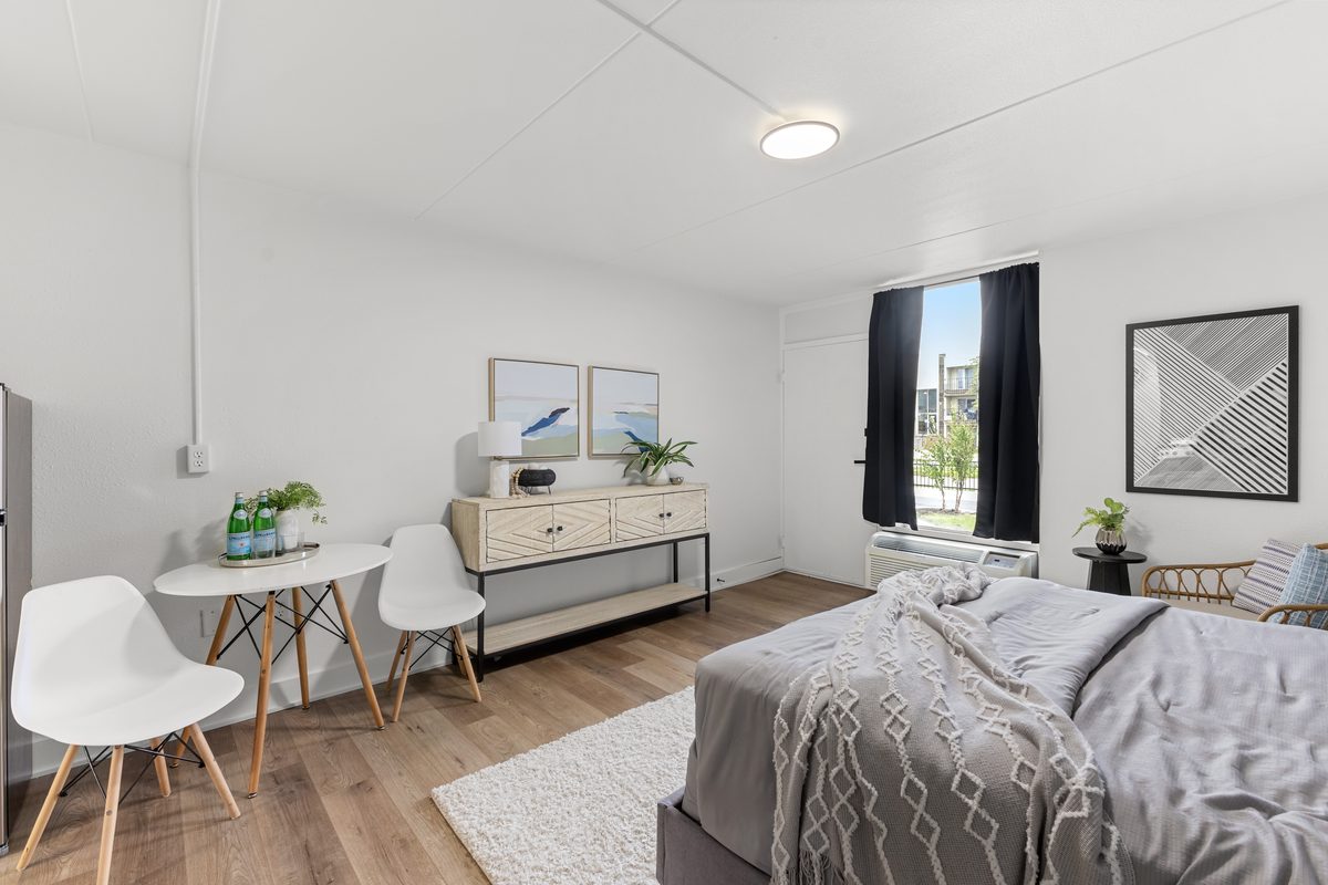 A studio apartment looking toward the window at the far wall, with a dining table for two and a dresser.