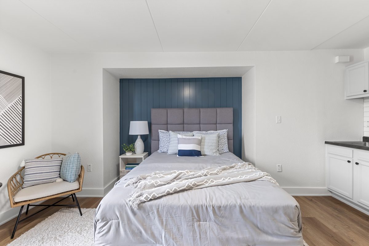 A queen bed against the navy vertical panelling, with a lamp and a lounge chair beside it.