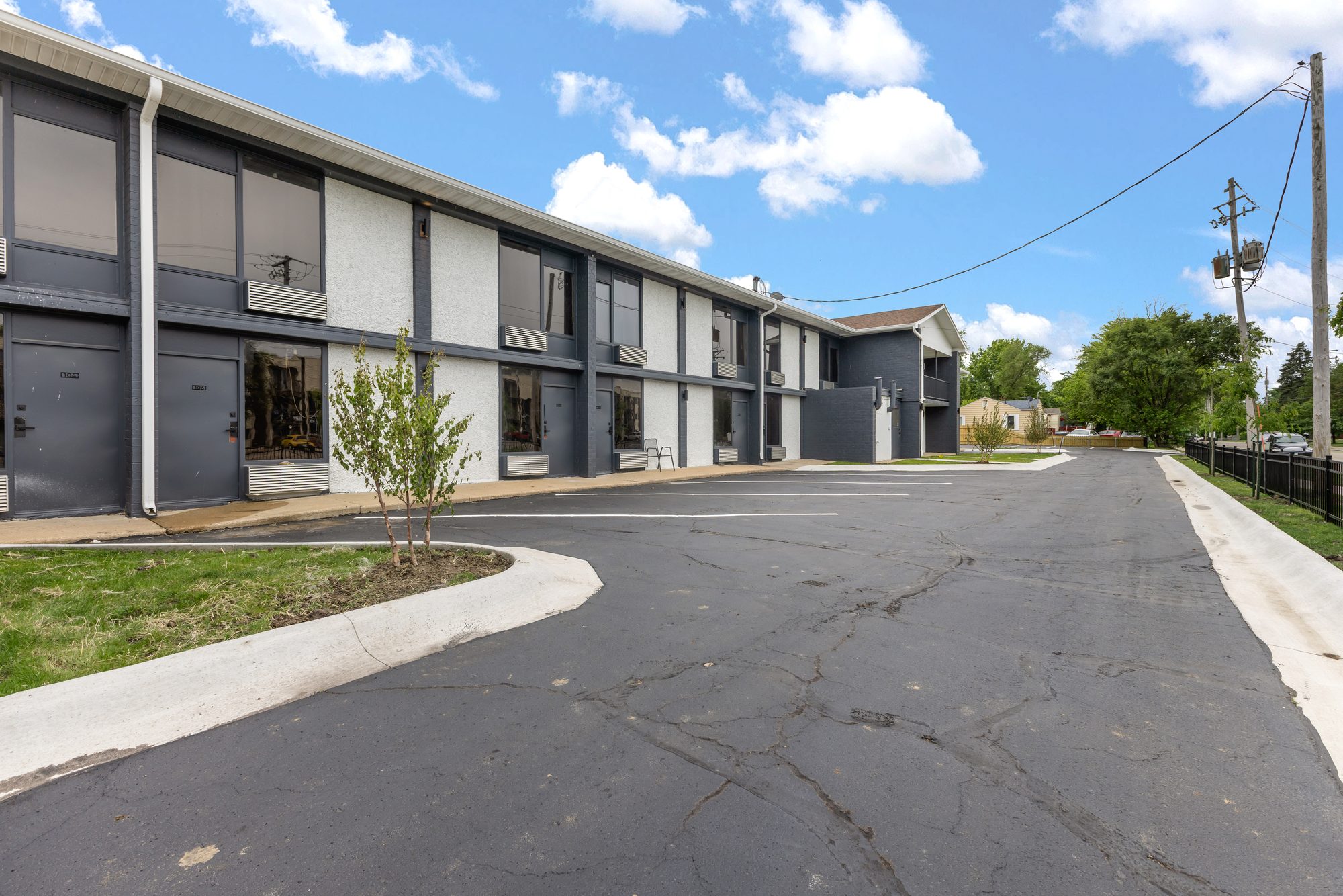The View on Douglas, a two-story apartment building with white stucco panels and charcoal brick, with ground floor apartments opening onto a freshly striped parking lot in Des Moines, Iowa.